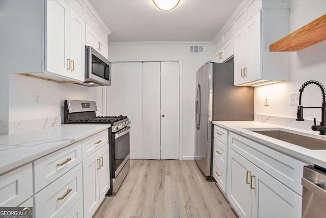 kitchen featuring stainless steel appliances, white cabinets, ornamental molding, light stone counters, and light hardwood / wood-style flooring