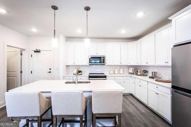 kitchen with appliances with stainless steel finishes, sink, decorative backsplash, dark hardwood / wood-style floors, and a kitchen island with sink