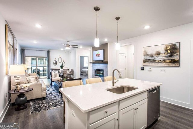 kitchen featuring stainless steel dishwasher, ceiling fan, an island with sink, sink, and dark wood-type flooring