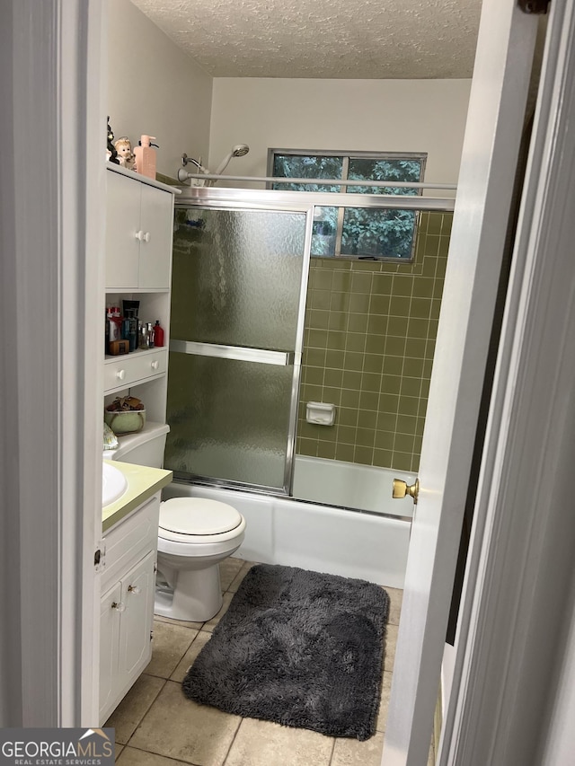 bathroom with a textured ceiling, combined bath / shower with glass door, vanity, and tile patterned floors