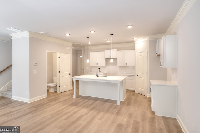 kitchen with white cabinets, sink, a center island with sink, decorative light fixtures, and light hardwood / wood-style floors