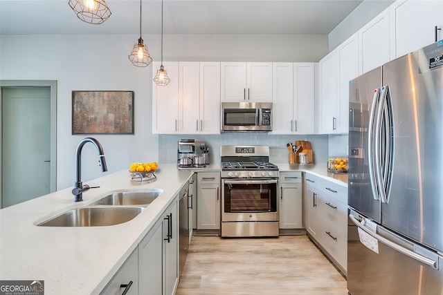 kitchen with pendant lighting, sink, appliances with stainless steel finishes, light hardwood / wood-style floors, and white cabinetry