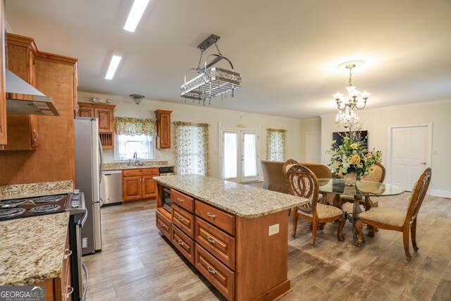 kitchen featuring wall chimney range hood, a chandelier, light wood-type flooring, light stone countertops, and appliances with stainless steel finishes