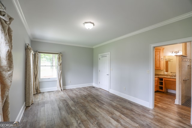 unfurnished bedroom featuring ensuite bath, wood-type flooring, and ornamental molding