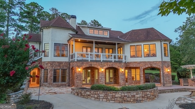 back house at dusk featuring a balcony and a patio area