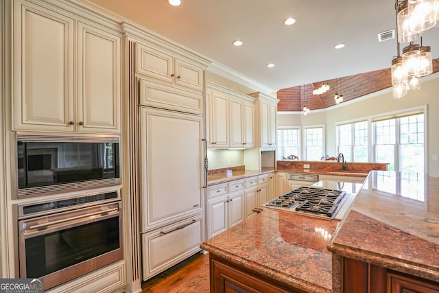 kitchen with built in appliances, light hardwood / wood-style flooring, light stone counters, cream cabinets, and ornamental molding