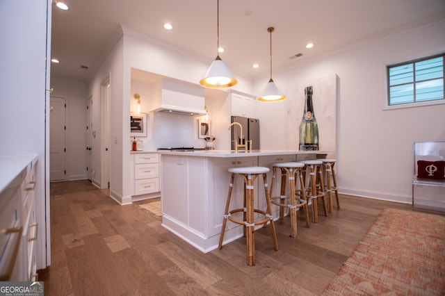 kitchen with light hardwood / wood-style floors, white cabinets, hanging light fixtures, and wall chimney exhaust hood