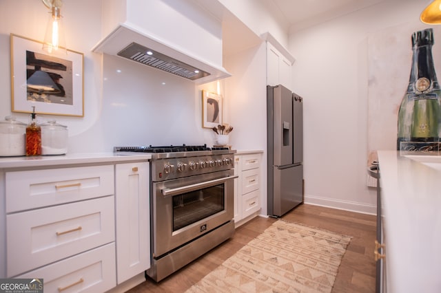 kitchen with light hardwood / wood-style floors, appliances with stainless steel finishes, white cabinetry, and premium range hood