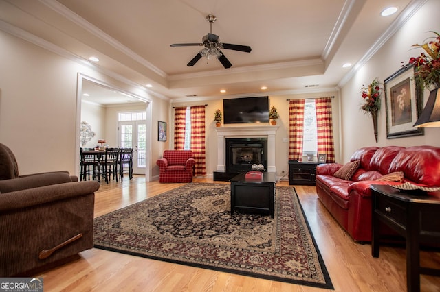 living room with a raised ceiling, ornamental molding, hardwood / wood-style flooring, and ceiling fan