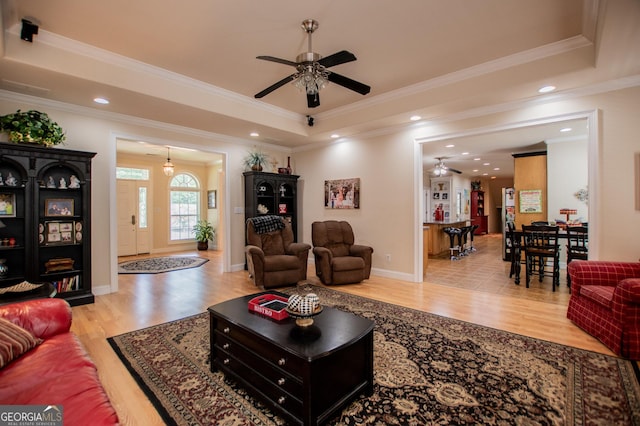 living room with ornamental molding, light wood-type flooring, and a tray ceiling