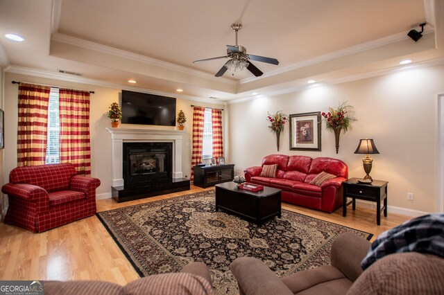 living room with hardwood / wood-style flooring, ornamental molding, ceiling fan, and a tray ceiling