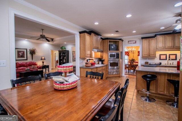 tiled dining space with ceiling fan, ornamental molding, a raised ceiling, and sink