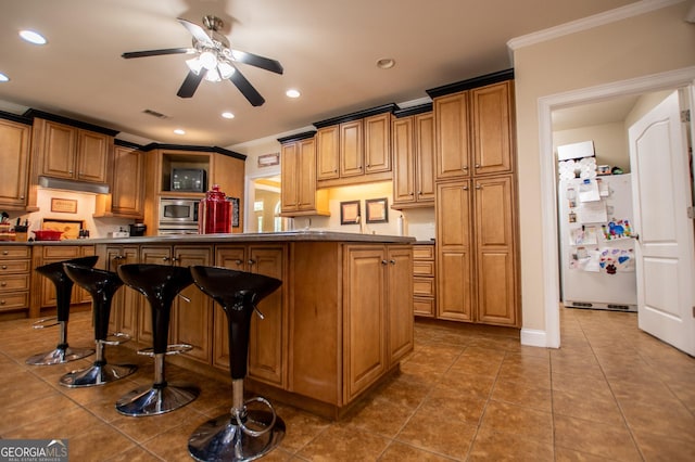 kitchen featuring ceiling fan, tile patterned flooring, white refrigerator, ornamental molding, and a kitchen bar