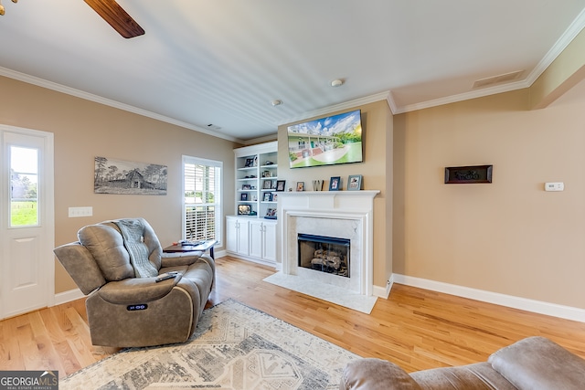 living room featuring built in features, light hardwood / wood-style flooring, a fireplace, and crown molding