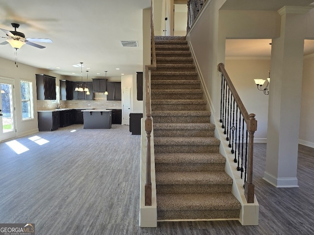 stairway featuring baseboards, visible vents, wood finished floors, and ceiling fan with notable chandelier