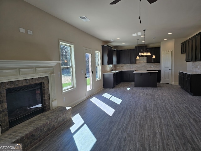 kitchen featuring a center island, a sink, light countertops, a fireplace, and backsplash