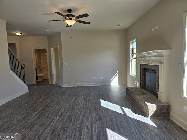 unfurnished living room with dark wood-style flooring, a ceiling fan, baseboards, stairs, and a brick fireplace