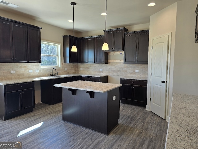 kitchen with light stone counters, visible vents, a center island, dark wood-style floors, and tasteful backsplash