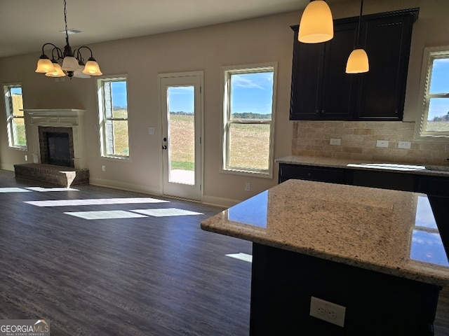 kitchen featuring a fireplace with raised hearth, dark cabinetry, dark wood finished floors, and tasteful backsplash