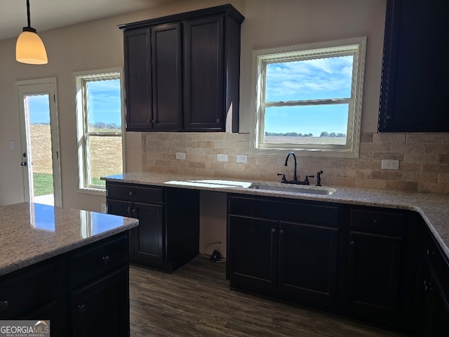 kitchen featuring light stone counters, dark wood-style flooring, hanging light fixtures, a sink, and backsplash