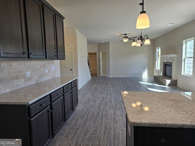 kitchen with visible vents, a fireplace with raised hearth, dark wood-style floors, open floor plan, and backsplash