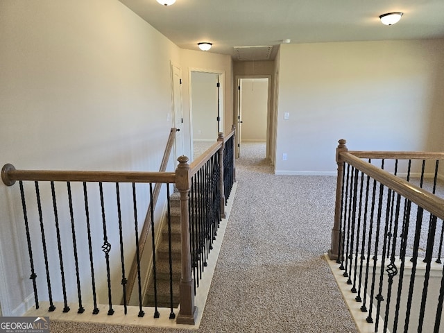 hallway with carpet floors, attic access, baseboards, and an upstairs landing