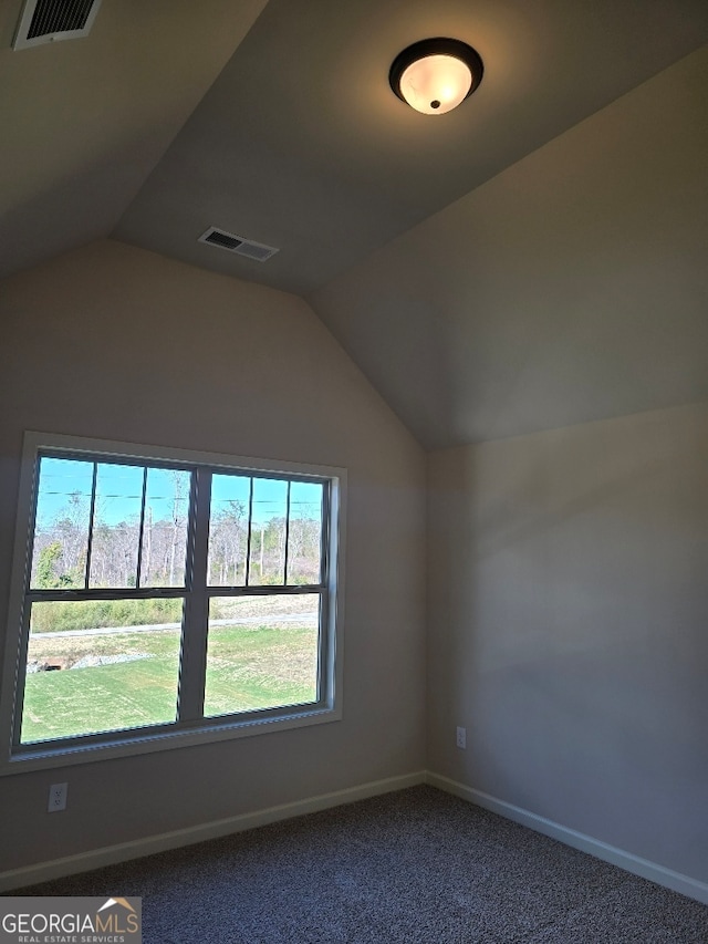 empty room with lofted ceiling, baseboards, visible vents, and dark colored carpet