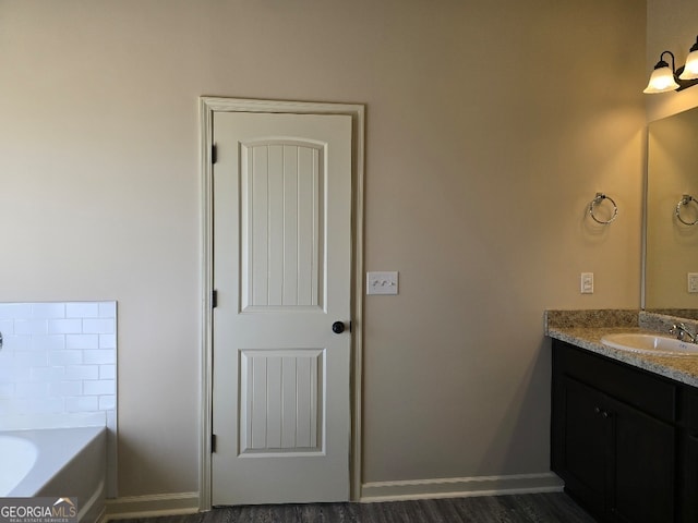 bathroom with baseboards, wood finished floors, a bath, and vanity