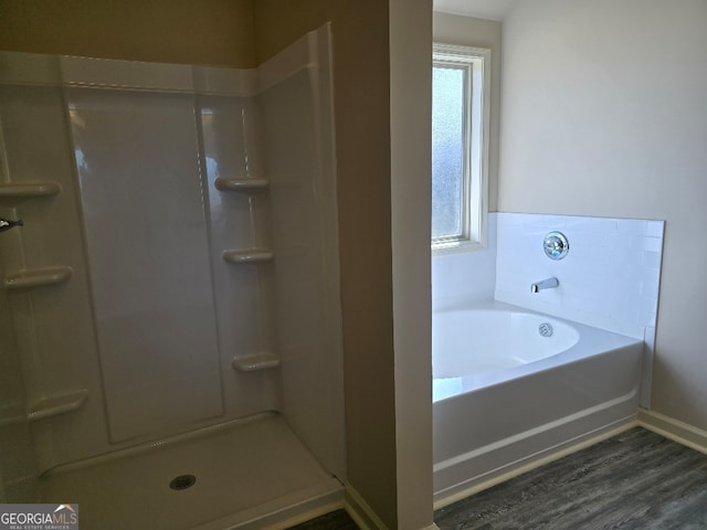 bathroom featuring baseboards, a shower stall, a bath, and wood finished floors