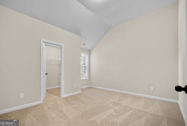 unfurnished bedroom featuring light carpet, lofted ceiling, a closet, and a walk in closet