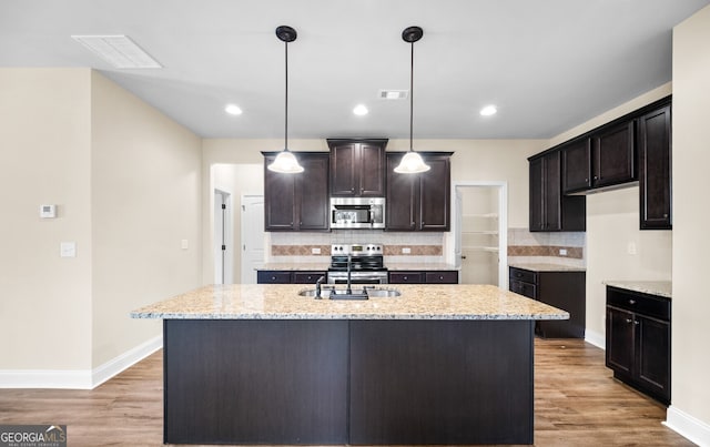 kitchen with pendant lighting, a kitchen island with sink, stainless steel appliances, and light hardwood / wood-style floors