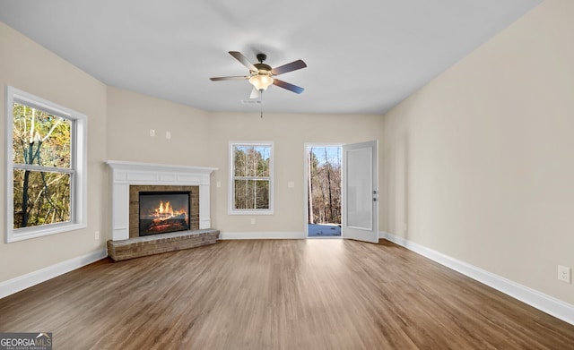 unfurnished living room featuring wood-type flooring, ceiling fan, and a brick fireplace