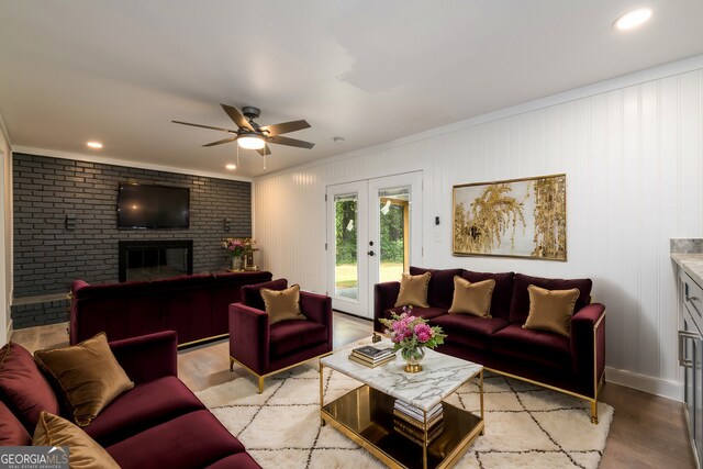 living room featuring crown molding, french doors, a brick fireplace, light hardwood / wood-style floors, and ceiling fan