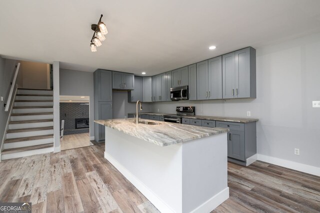 kitchen featuring a kitchen island with sink, appliances with stainless steel finishes, hardwood / wood-style floors, and light stone countertops