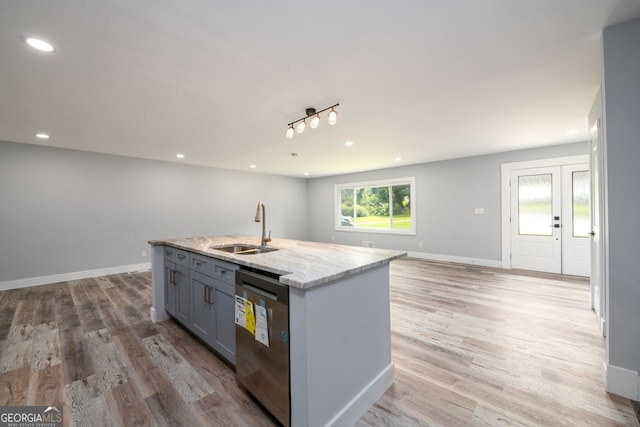 kitchen featuring dishwasher, light hardwood / wood-style floors, a kitchen island with sink, sink, and light stone counters