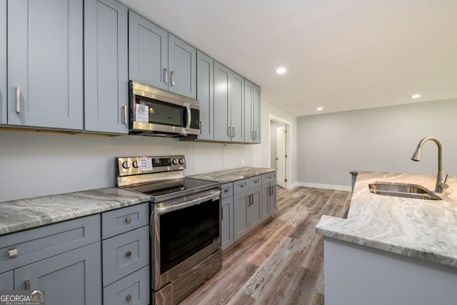 kitchen with appliances with stainless steel finishes, dark hardwood / wood-style flooring, light stone counters, and sink