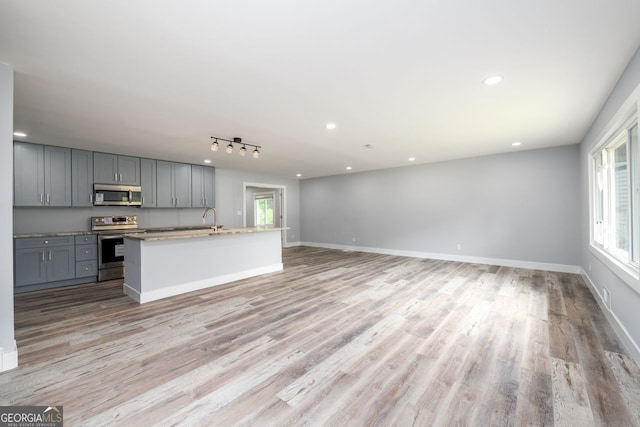 kitchen featuring light wood-type flooring, appliances with stainless steel finishes, gray cabinets, and a center island with sink