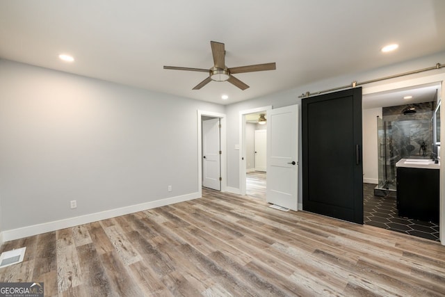 unfurnished bedroom featuring a barn door, hardwood / wood-style floors, and ensuite bath