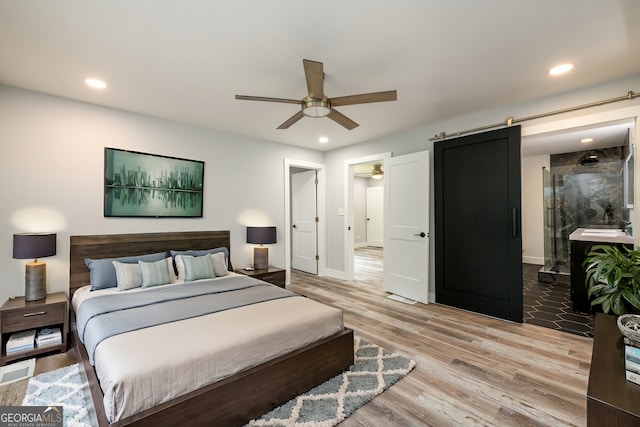 bedroom featuring hardwood / wood-style floors, ceiling fan, and a barn door