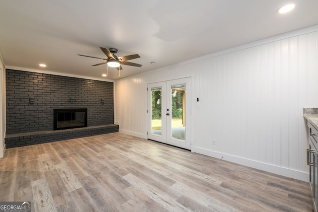 unfurnished living room featuring french doors, light hardwood / wood-style floors, crown molding, a brick fireplace, and ceiling fan