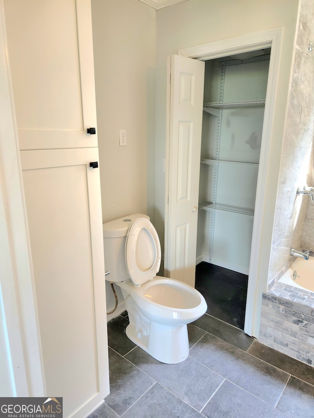 bathroom with tiled tub, tile patterned floors, and toilet