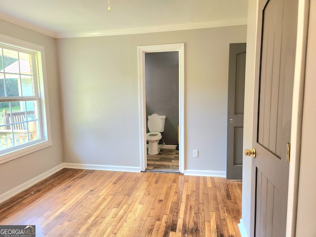 unfurnished bedroom featuring ornamental molding, multiple windows, ensuite bath, and light wood-type flooring