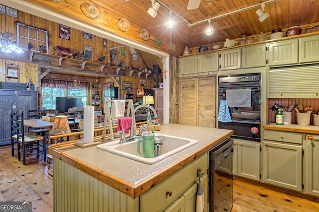 kitchen featuring wood walls, an island with sink, light hardwood / wood-style floors, black appliances, and sink