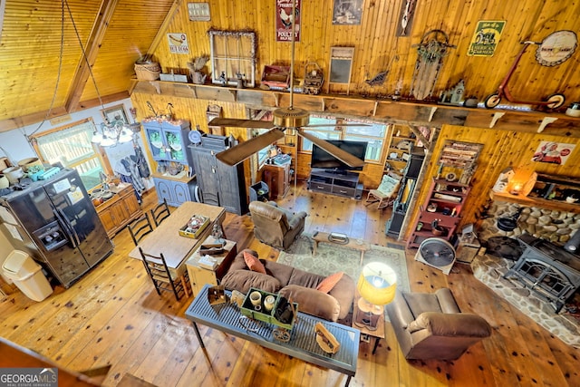 living room with wooden walls, hardwood / wood-style flooring, vaulted ceiling, and a wood stove