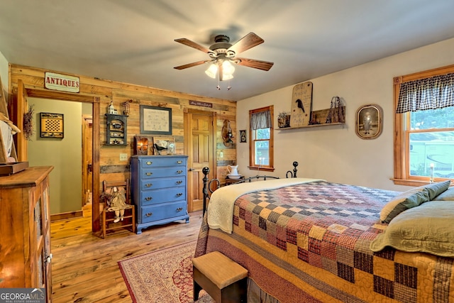 bedroom featuring light hardwood / wood-style floors, ceiling fan, and wooden walls