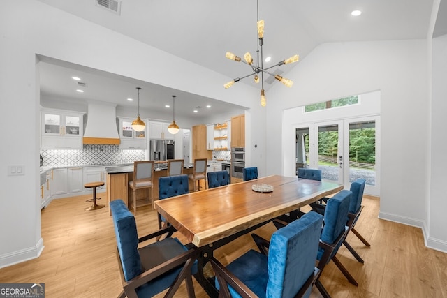 dining area featuring high vaulted ceiling, a chandelier, light wood-type flooring, and french doors