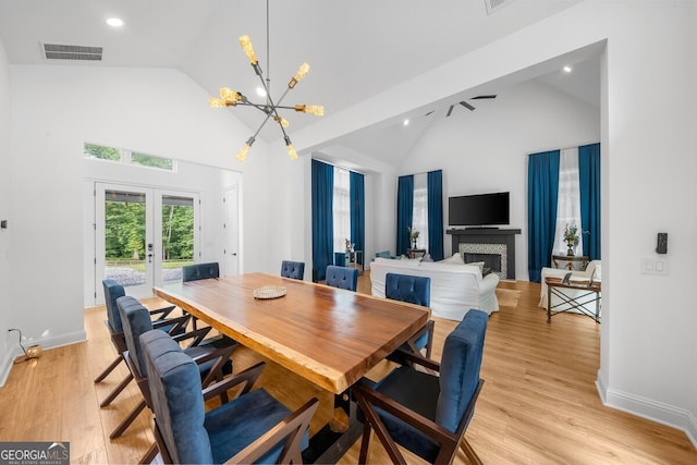 dining area with french doors, light wood-type flooring, an inviting chandelier, a tile fireplace, and high vaulted ceiling