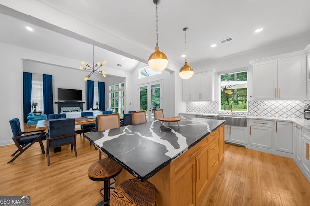 kitchen featuring decorative backsplash, white cabinets, light wood-type flooring, sink, and a center island