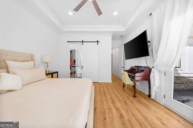 bedroom featuring a tray ceiling, light hardwood / wood-style floors, a barn door, and ceiling fan