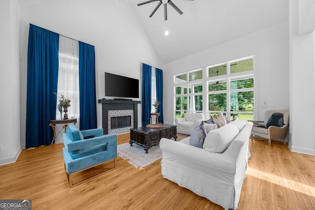 living room featuring a tile fireplace, high vaulted ceiling, ceiling fan, and light hardwood / wood-style flooring